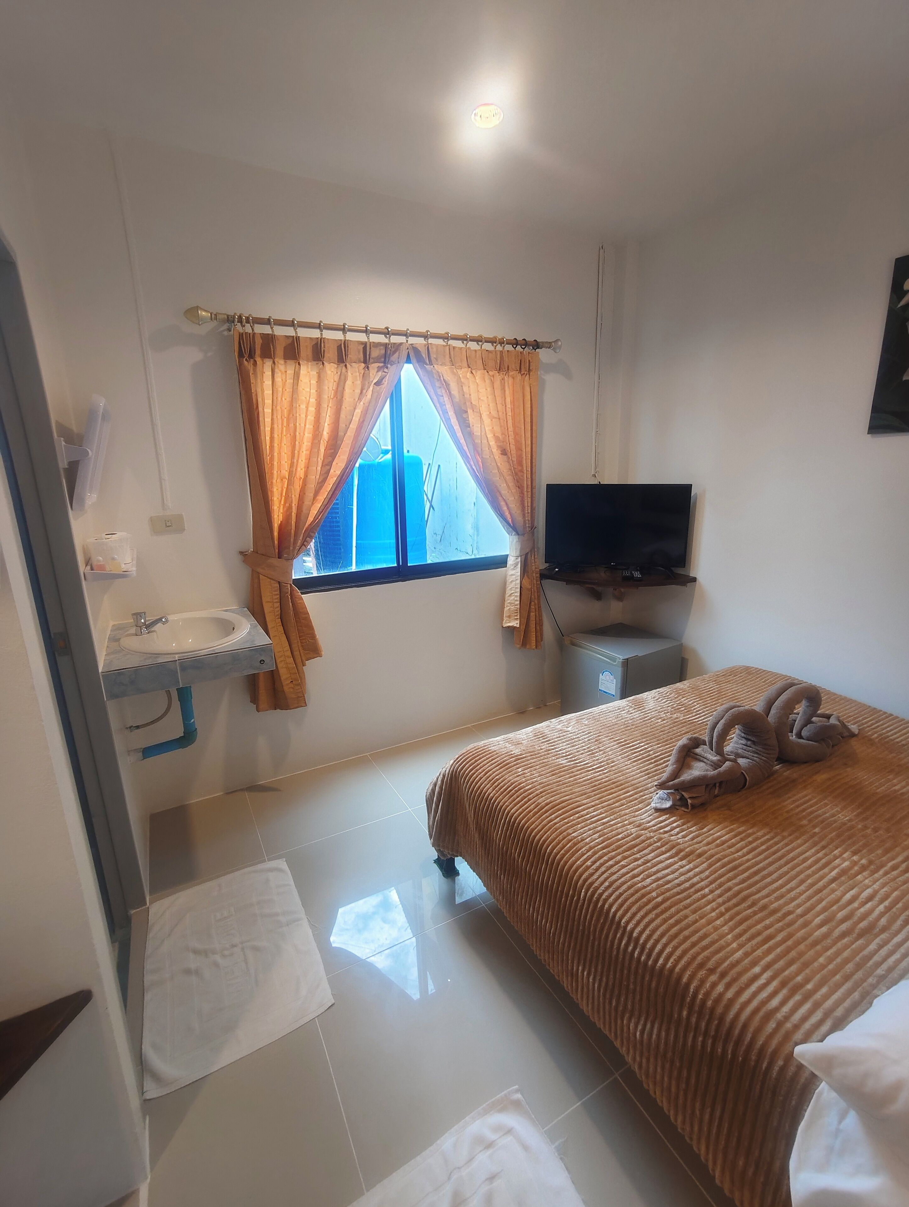 A bedroom with a bed, a TV, a window with curtains, a sink, and a mirror.