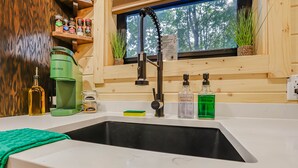 A kitchen with a black sink, a green coffee maker, and various kitchen items on the counter. - The Hocking Hills Treehouse (Rockbridge)