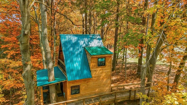 A wooden cabin with a blue roof, surrounded by autumn foliage. - The Hocking Hills Treehouse (Rockbridge)