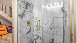 A bathroom with marble walls, a shower with a gold handle, and a visible step. - Pikachu's Palace Treehouse (Rockbridge)