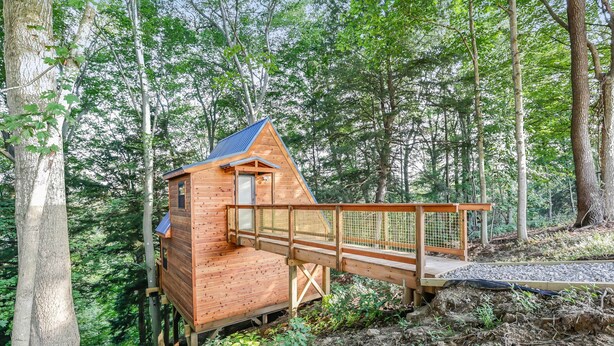 A wooden cabin with a sloped roof, elevated on stilts, connected to the ground by a wooden bridge. - Pikachu's Palace Treehouse (Rockbridge)