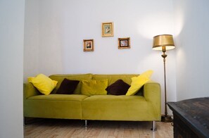 Um quarto com um sofá verde, um abajur e três quadros na parede.