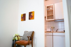 Um quarto com uma cadeira de madeira, um vaso com flores e duas pinturas penduradas na parede.