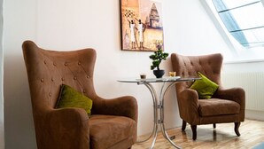 Two brown armchairs with green cushions, a small table with a potted plant, and a painting on the wall.