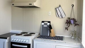 A kitchen with a white stove, a hanging pot rack with kitchen utensils, and a window with a view. - The Nest on Till (Oamaru)