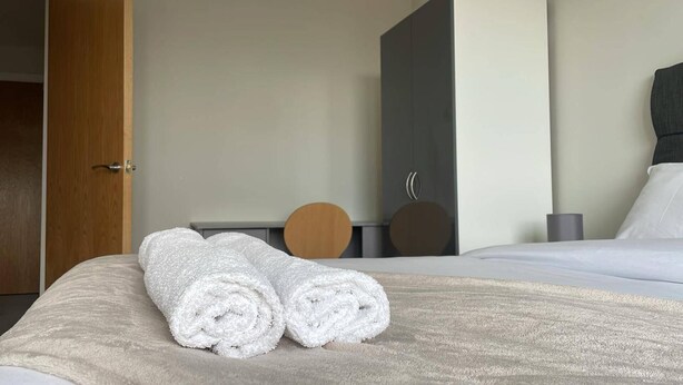 A hotel room with a neatly made bed, a wooden chair, a desk, and a large mirror. - Apartment - Sleeps 4, Pets Allowed & Parking (Salford)