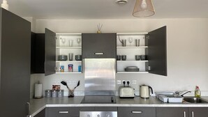 A modern kitchen with open cabinets, a stainless steel refrigerator, a toaster, a kettle, and a sink. - Apartment - Sleeps 4, Pets Allowed & Parking (Salford)