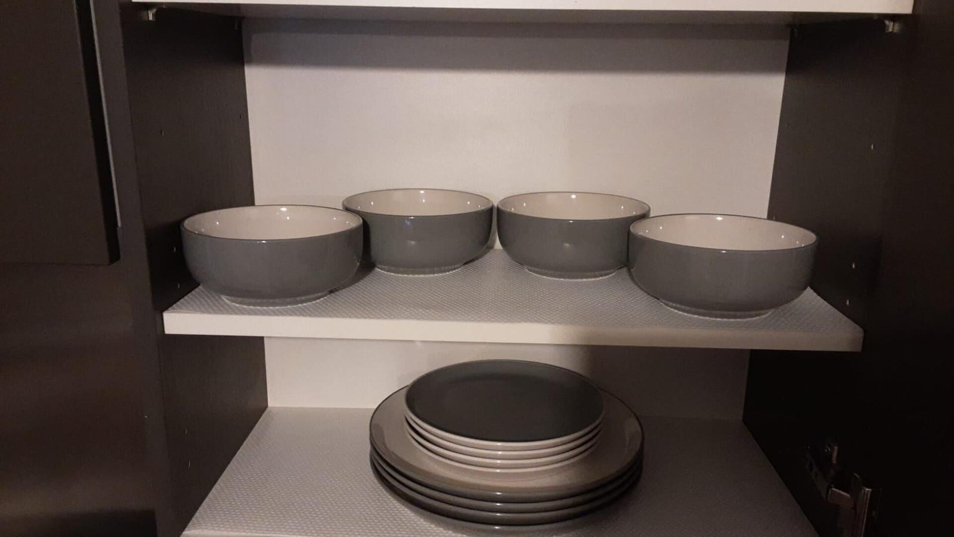 Un estante de cocina con cuatro cuencos grises y una pila de platos.