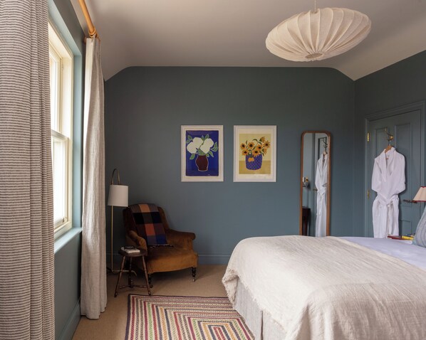 Une chambre à coucher avec un lit, une chaise, un miroir et deux tableaux encadrés accrochés au mur.