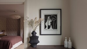 Ein Schlafzimmer mit einem Bett, einer Vase mit getrockneten Blumen, einem gerahmten Kunstwerk und zwei Flaschen auf einem Regal.