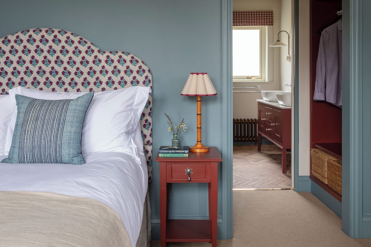 A bedroom with a bed, bedside table, lamp, and a view into the bathroom.