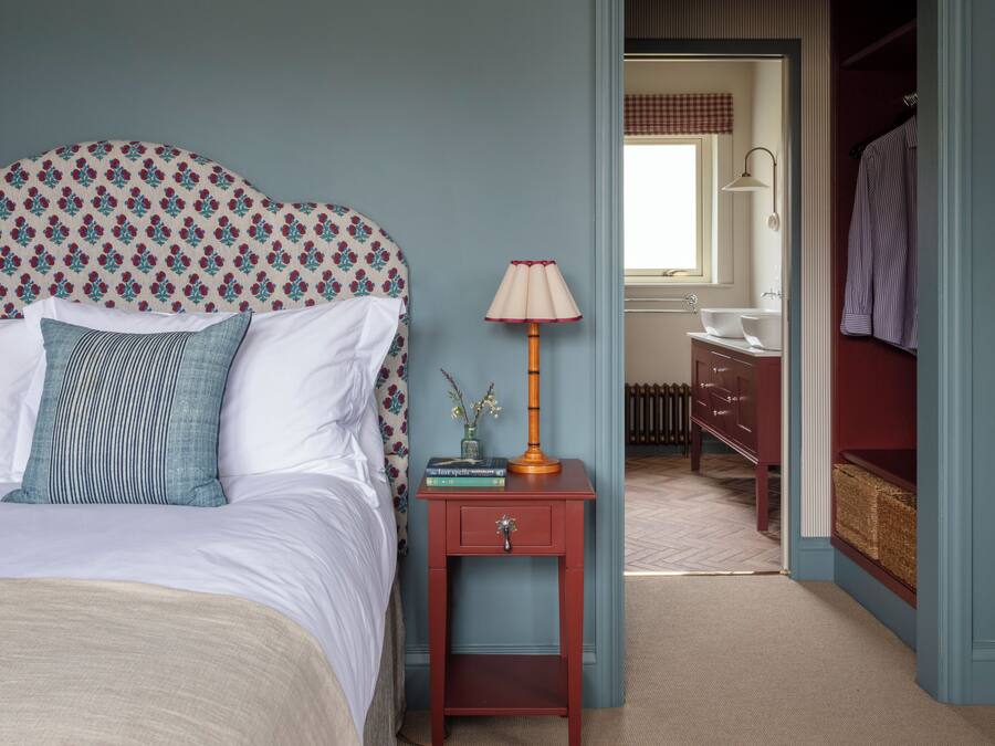 A bedroom with a bed, bedside table, lamp, and a view into the bathroom.