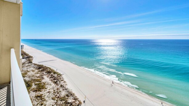 A beach view from a balcony with a clear sky and sun shining on the ocean.