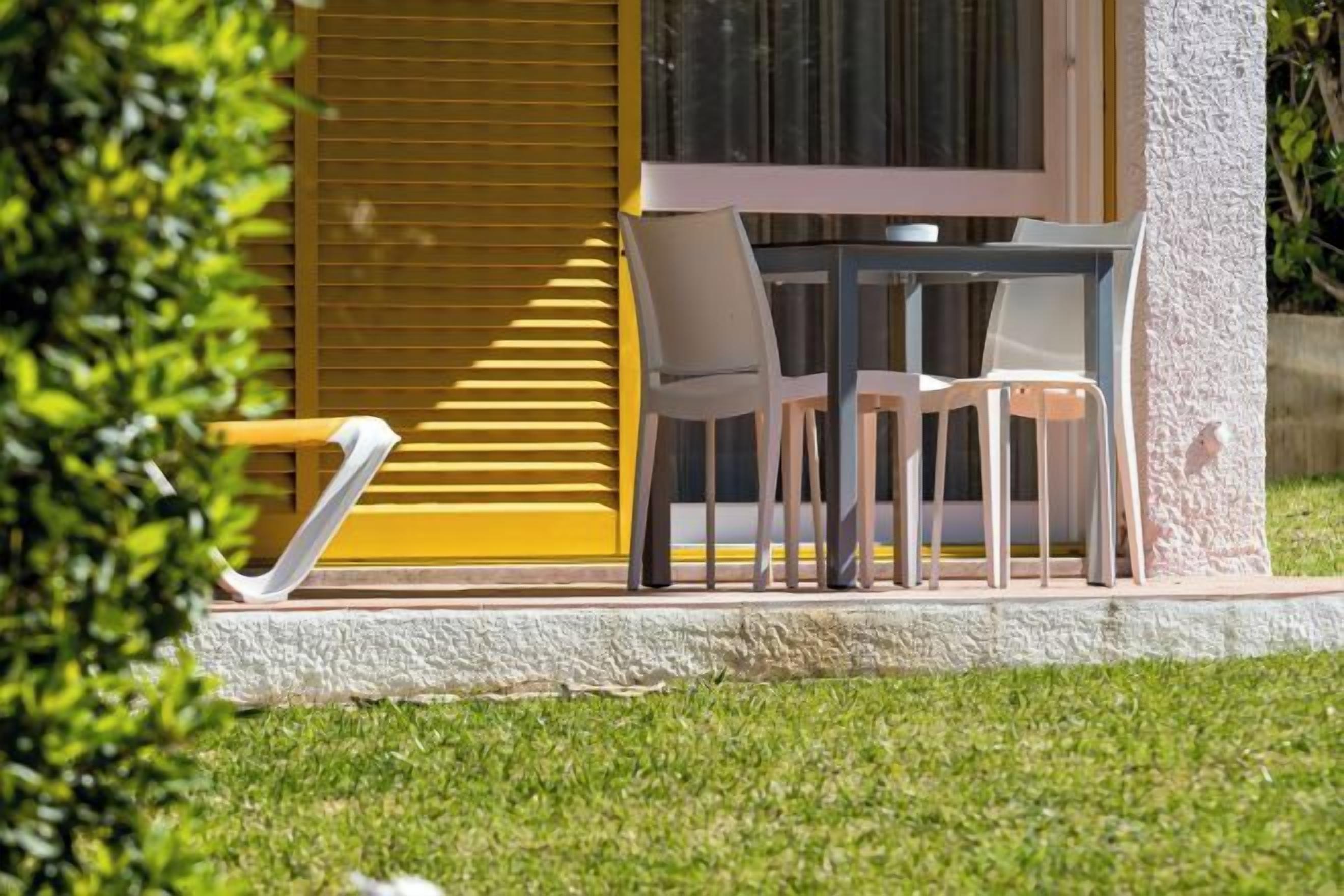 A yellow building with a porch, a table, and two chairs.