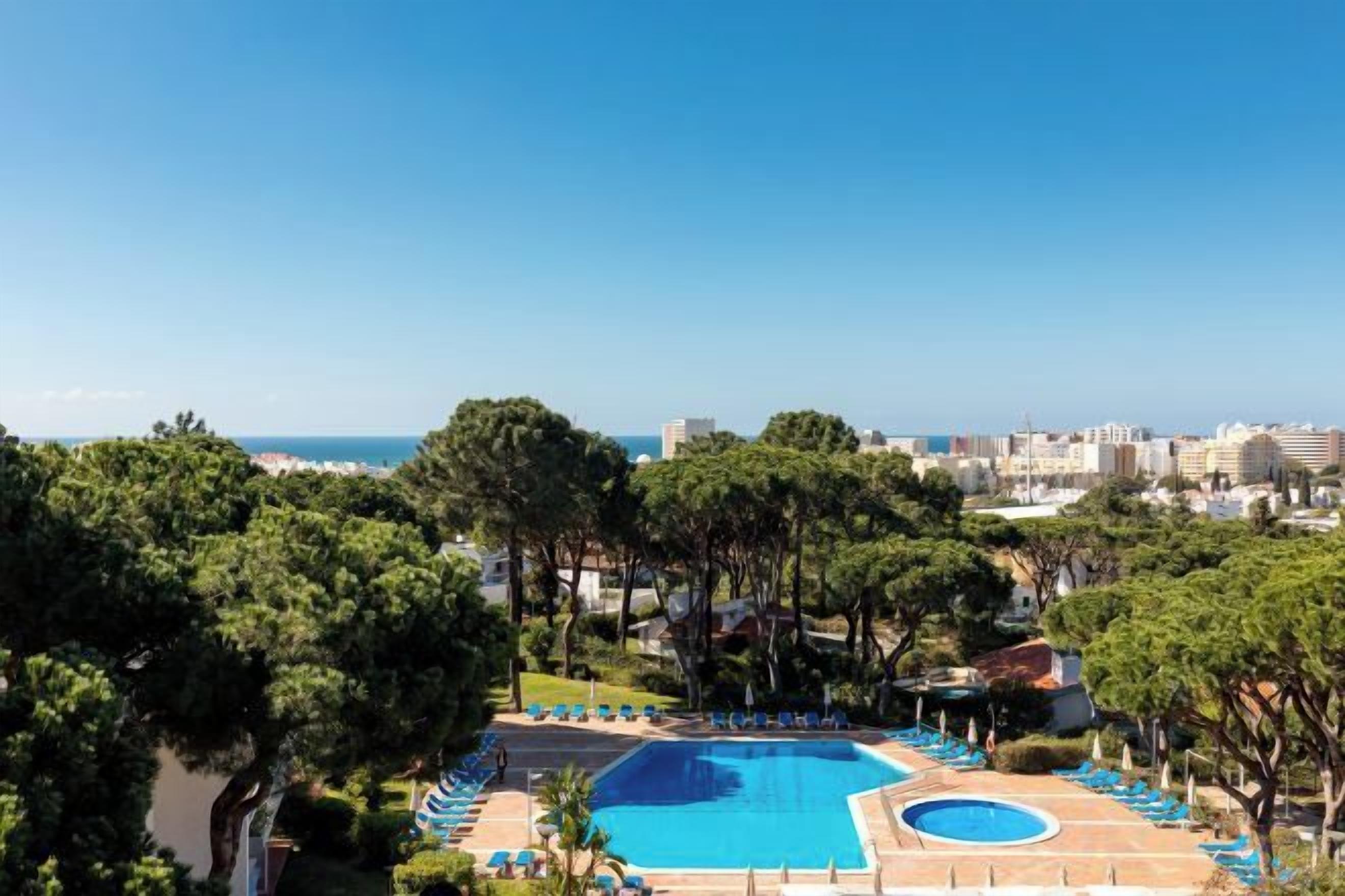 A pool area with a view of the sea, surrounded by trees and buildings.