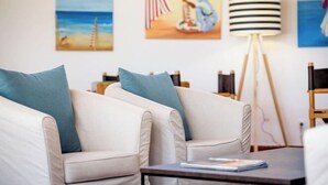 Un salon avec deux canapés beige, une petite table sur laquelle repose un magazine et un lampadaire.