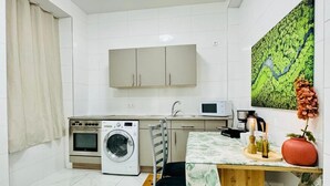 A compact kitchen with a washing machine, microwave, and a table with a vase and candles.