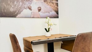 A dining area with a wooden table, chairs, a vase with flowers, and a large framed picture of a lake.