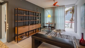 A modern living room with a large bookshelf, a dining area, and a balcony with a view.