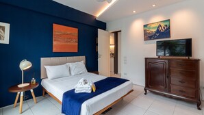 A bedroom with a bed, bedside table, lamp, dresser, and artwork on the walls.