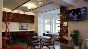 Un comedor moderno con mesas y sillas redondas, un sofá rojo y un televisor mostrando una película.