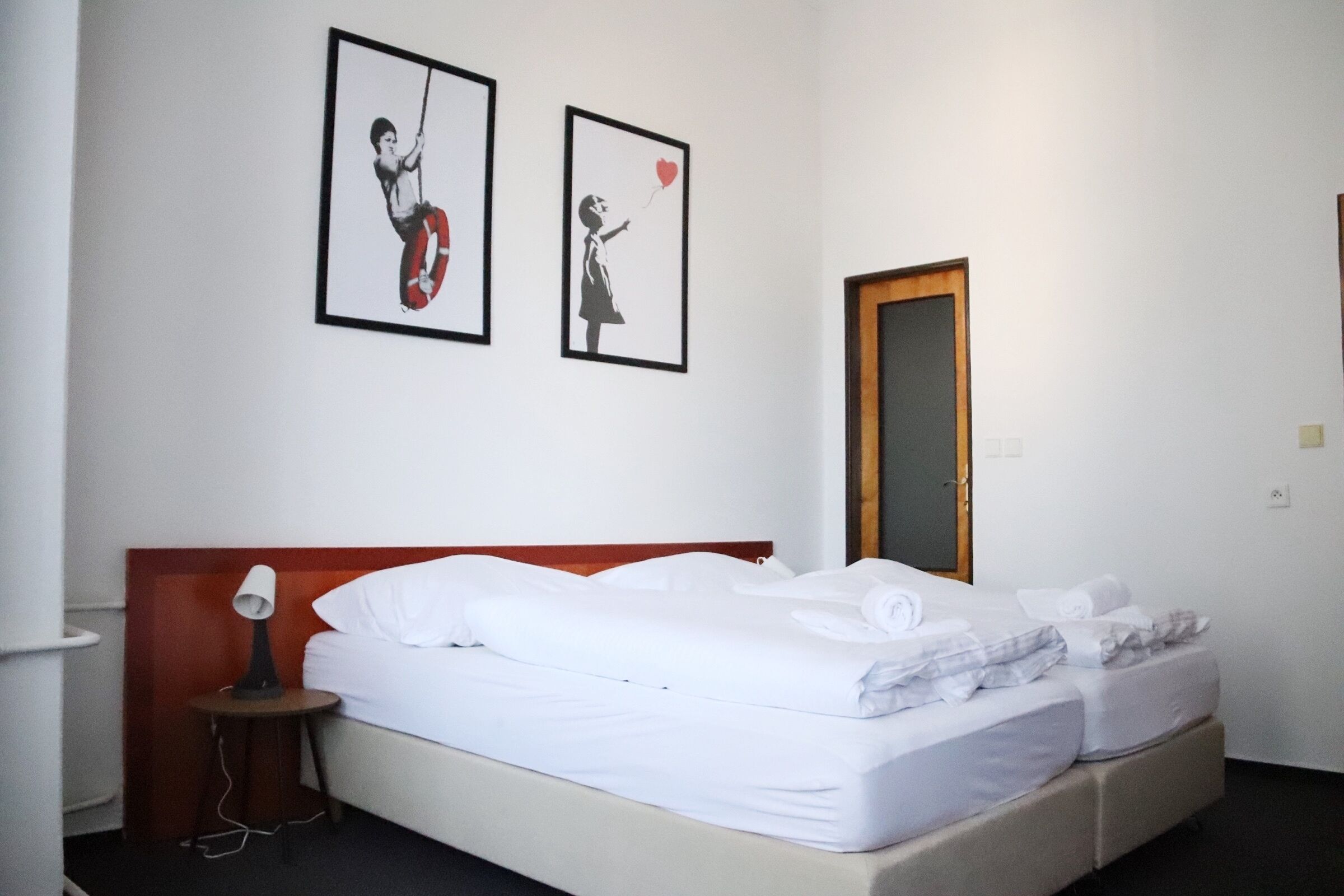 A hotel room with a bed, a bedside table with a lamp, and two framed pictures on the wall.