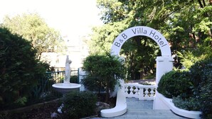 Entrada a B&B Villa Hotel, con un arco blanco, una estatua y un camino de jardín.