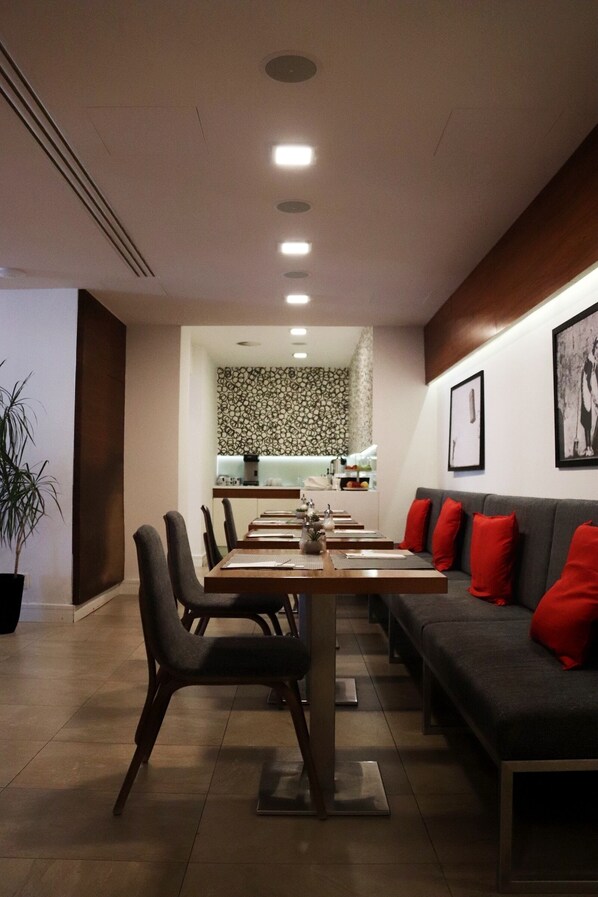 Un espace repas moderne avec une longue table, des chaises et un canapé agrémenté de coussins rouges.