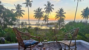 A beachside seating area with two chairs and a table, overlooking a sunset and palm trees. - KAE2 (Michamvi)