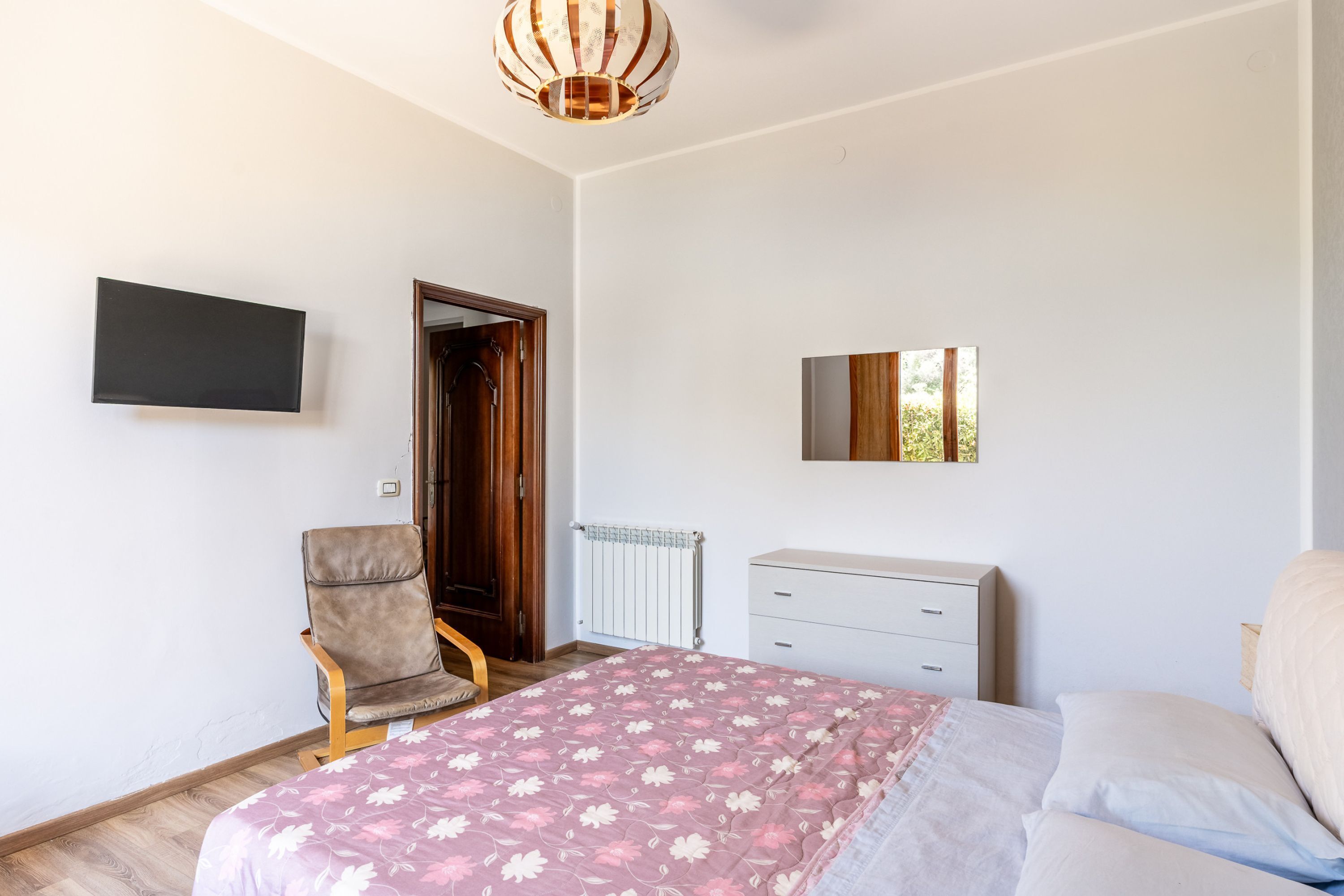 A bedroom with a bed, a chair, a dresser, a TV, and a mirror.