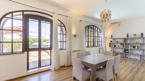 A spacious room with a large wooden dining table, white chairs, and a bookshelf filled with books and decorative items. - Casa Matilde Vista Mare con Piscina by Wonderful Italy (Syracuse)