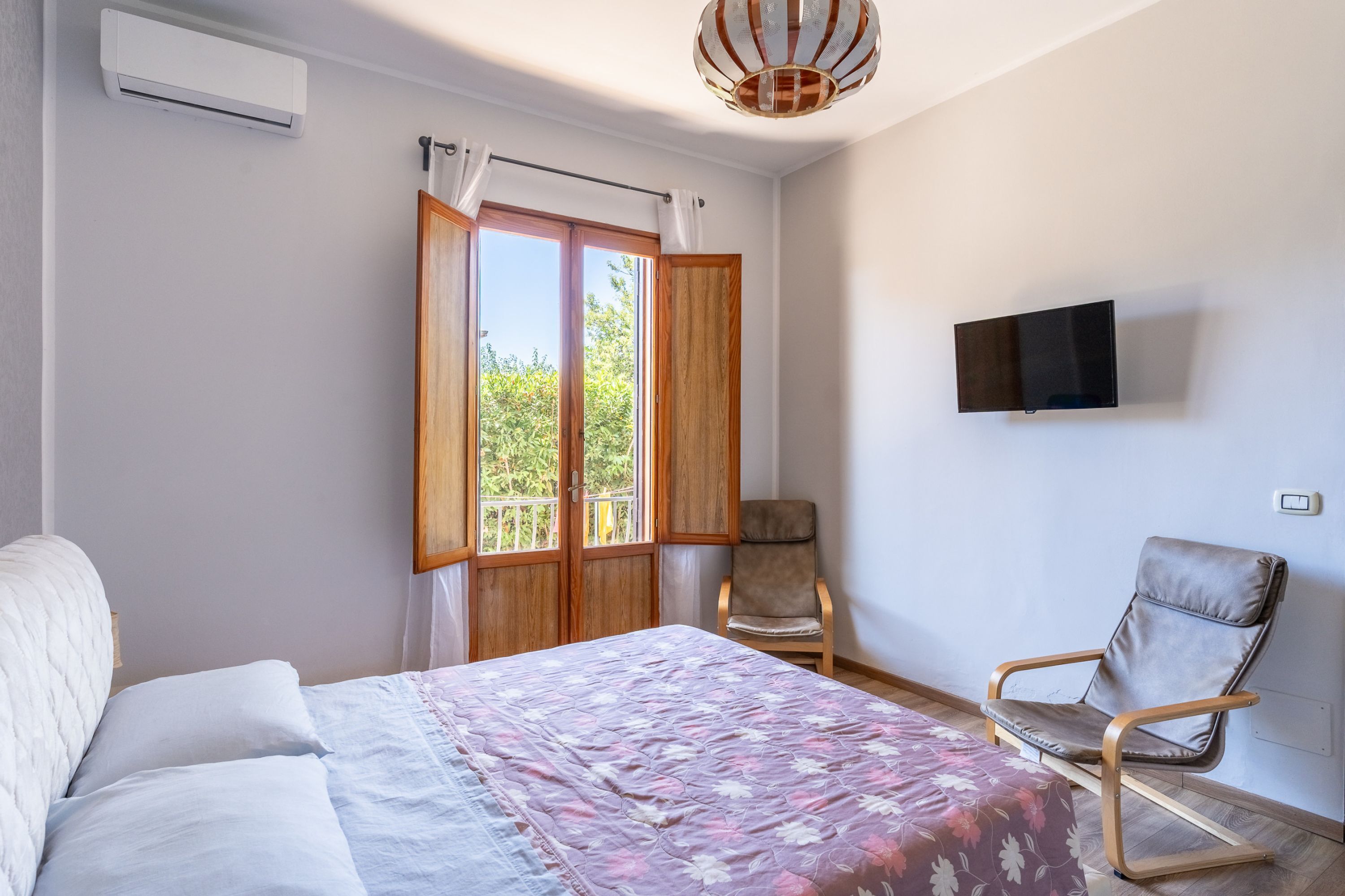 Une chambre à coucher avec un lit, une chaise, un téléviseur et une fenêtre avec des rideaux.