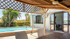 A wooden deck with a pool, outdoor seating, and a covered area with a lattice ceiling. - Casa Matilde Vista Mare con Piscina by Wonderful Italy (Syracuse)