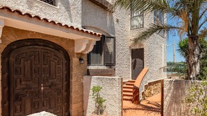 A stone building with a large wooden door, a small potted plant, and a staircase leading to a door. - Casa Matilde Vista Mare con Piscina by Wonderful Italy (Syracuse)