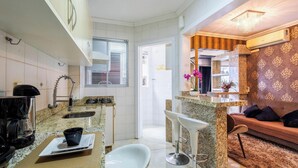A compact kitchen with a coffee maker, a sink, and a window with blinds.