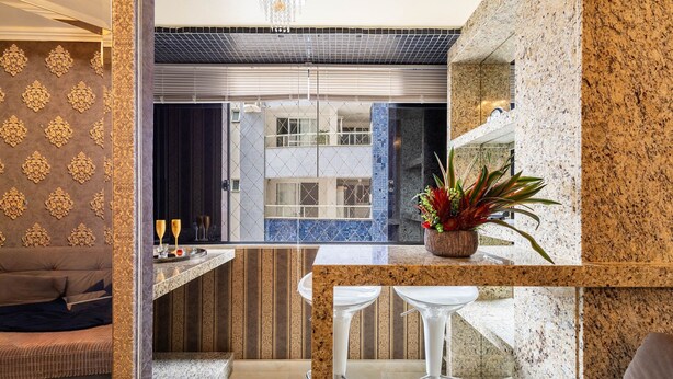 A modern kitchen with a marble countertop, two bar stools, and a potted plant.