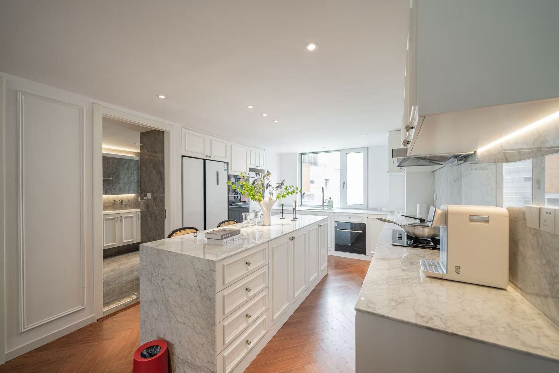 Une cuisine moderne avec des meubles blancs, un îlot en marbre et une cuisinière intégrée.