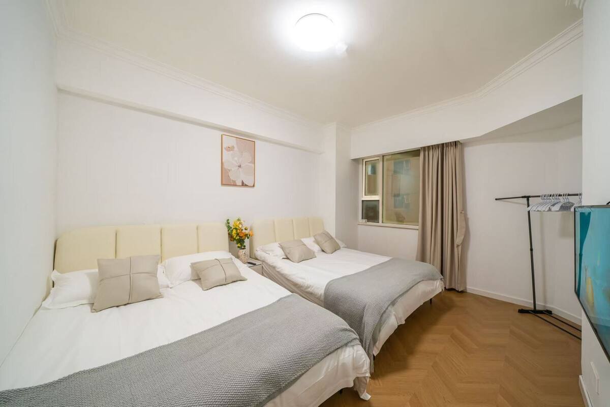 A hotel room with two beds, a window with curtains, a standing lamp, and a framed picture on the wall.
