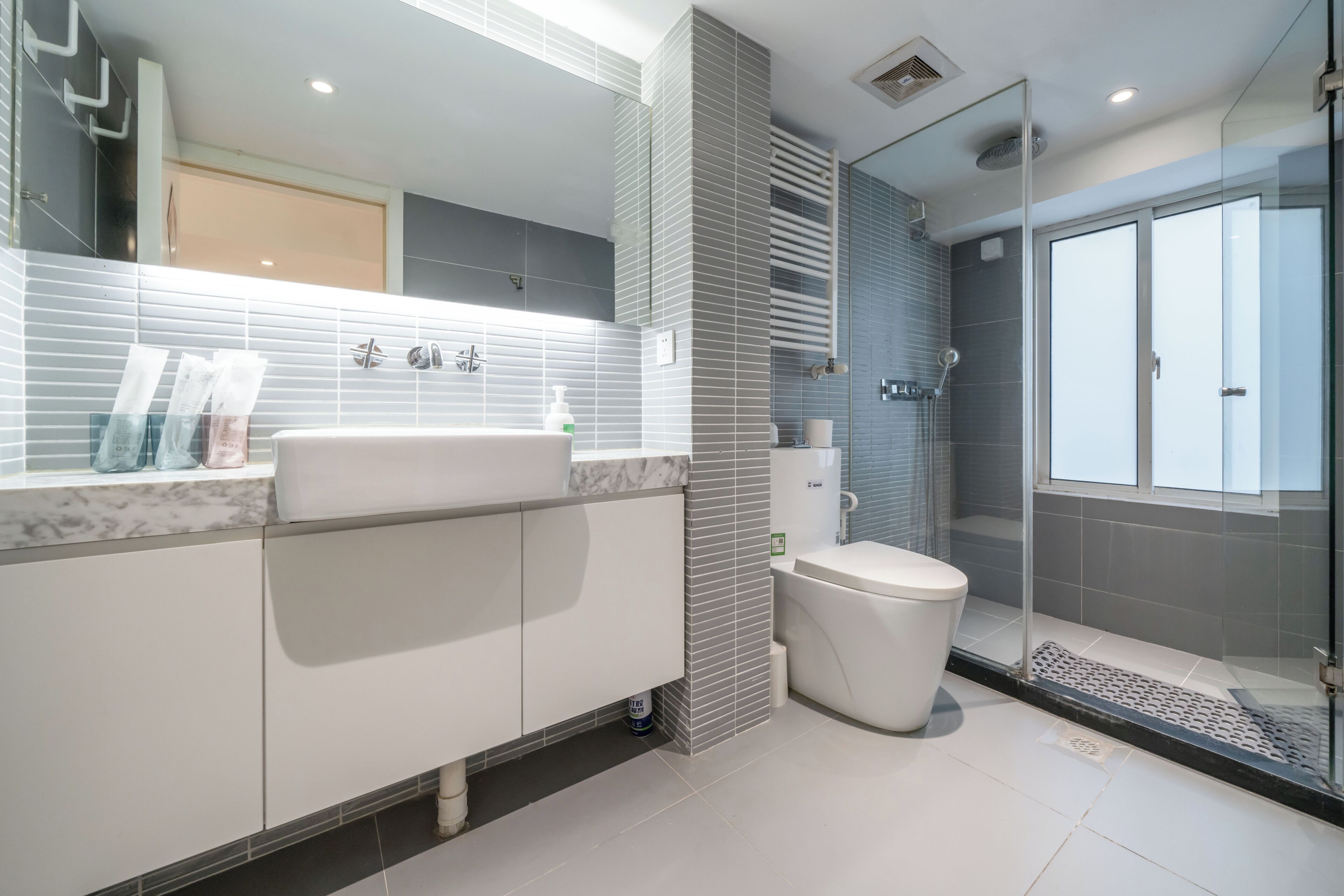 A modern bathroom with a large mirror, a white sink, a toilet, and a glass-enclosed shower area.