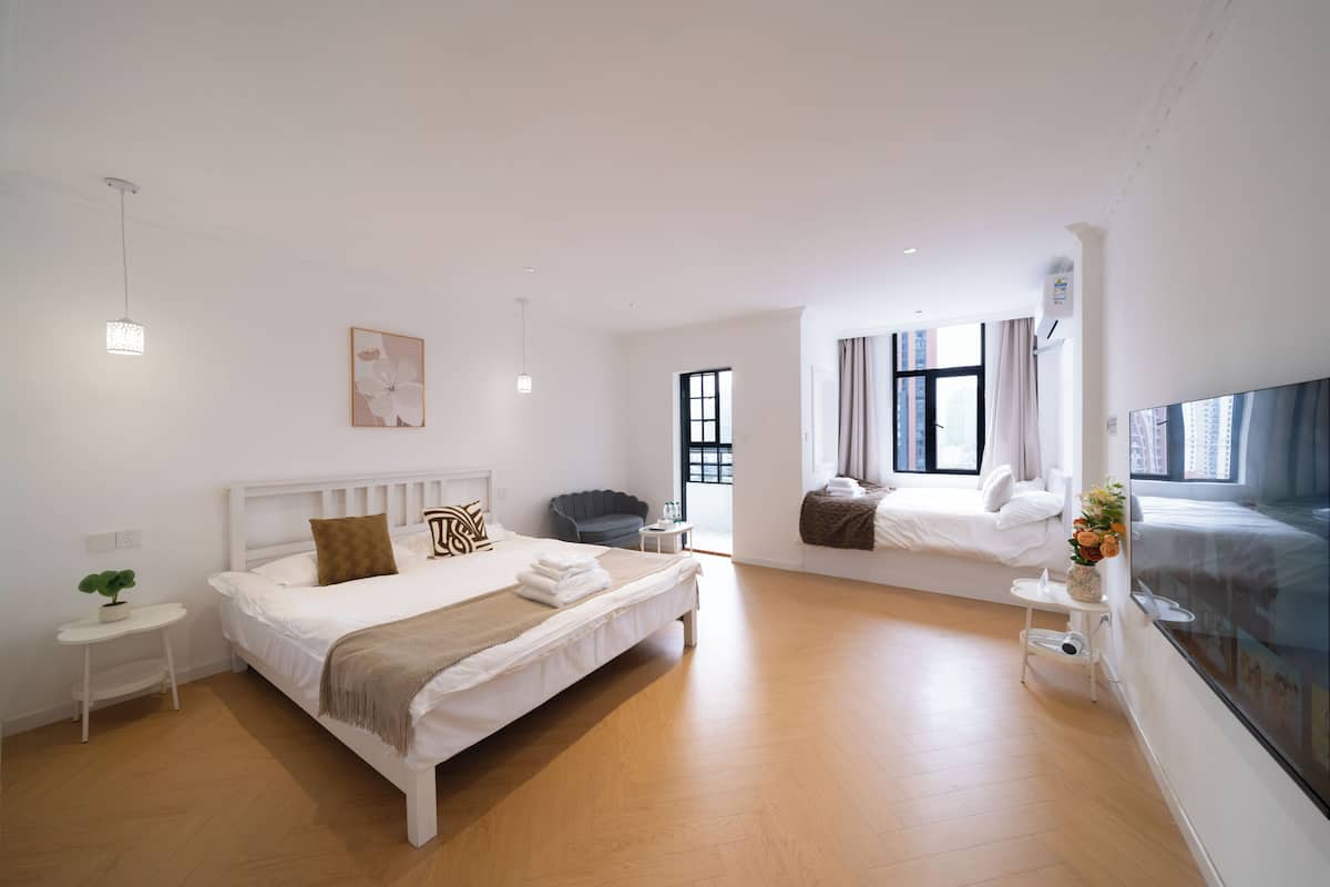 A modern hotel room with a large bed, a small side table, a chair, a window with curtains, and a view of the city.