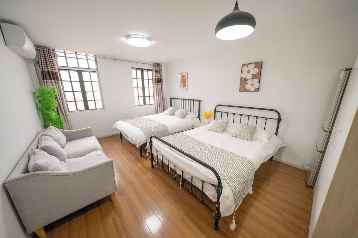 A bedroom with two beds, a sofa, and a window with curtains.