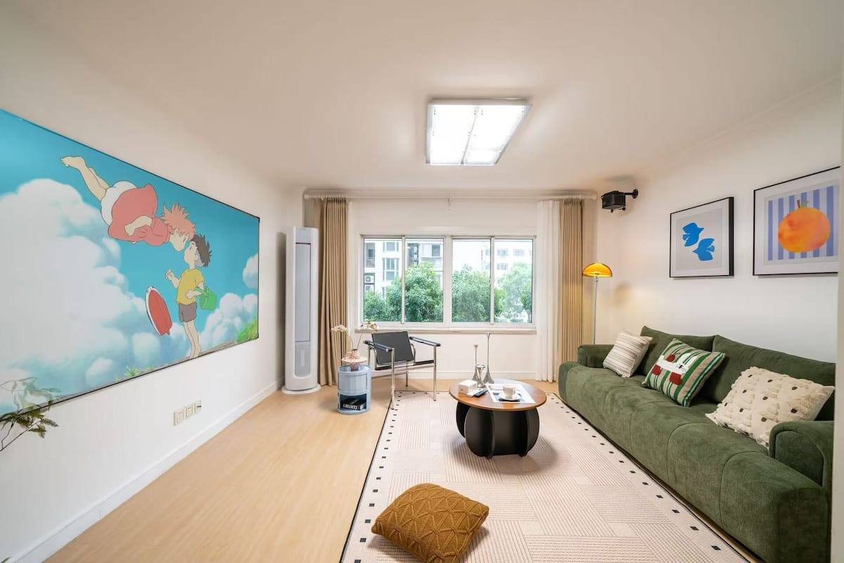 A living room with a green sofa, a coffee table, a large painting, and a window with a view of buildings.