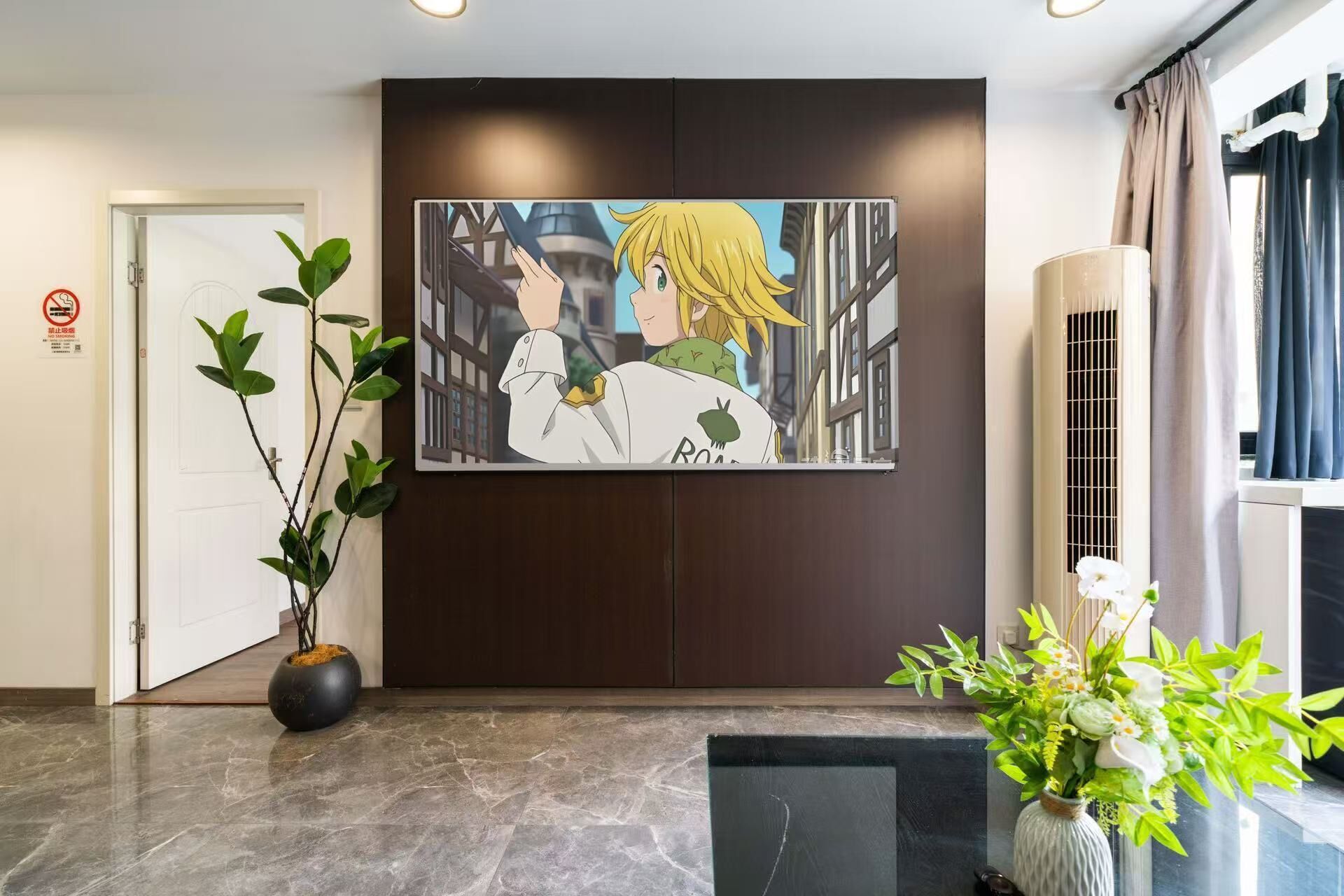 Eine Hotelhalle mit gerahmtem Anime-Kunstwerk, einer Zimmerpflanze, einer Vase mit Blumen und einer schwarzen Matte auf dem Boden.
