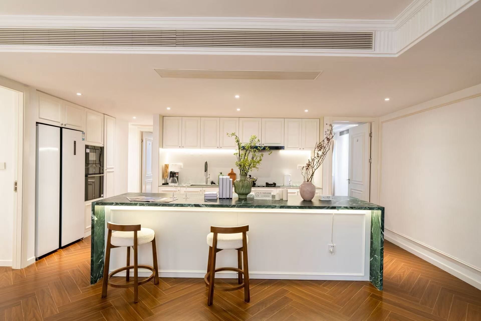 A modern kitchen with a marble island, two bar stools, and a built-in oven.