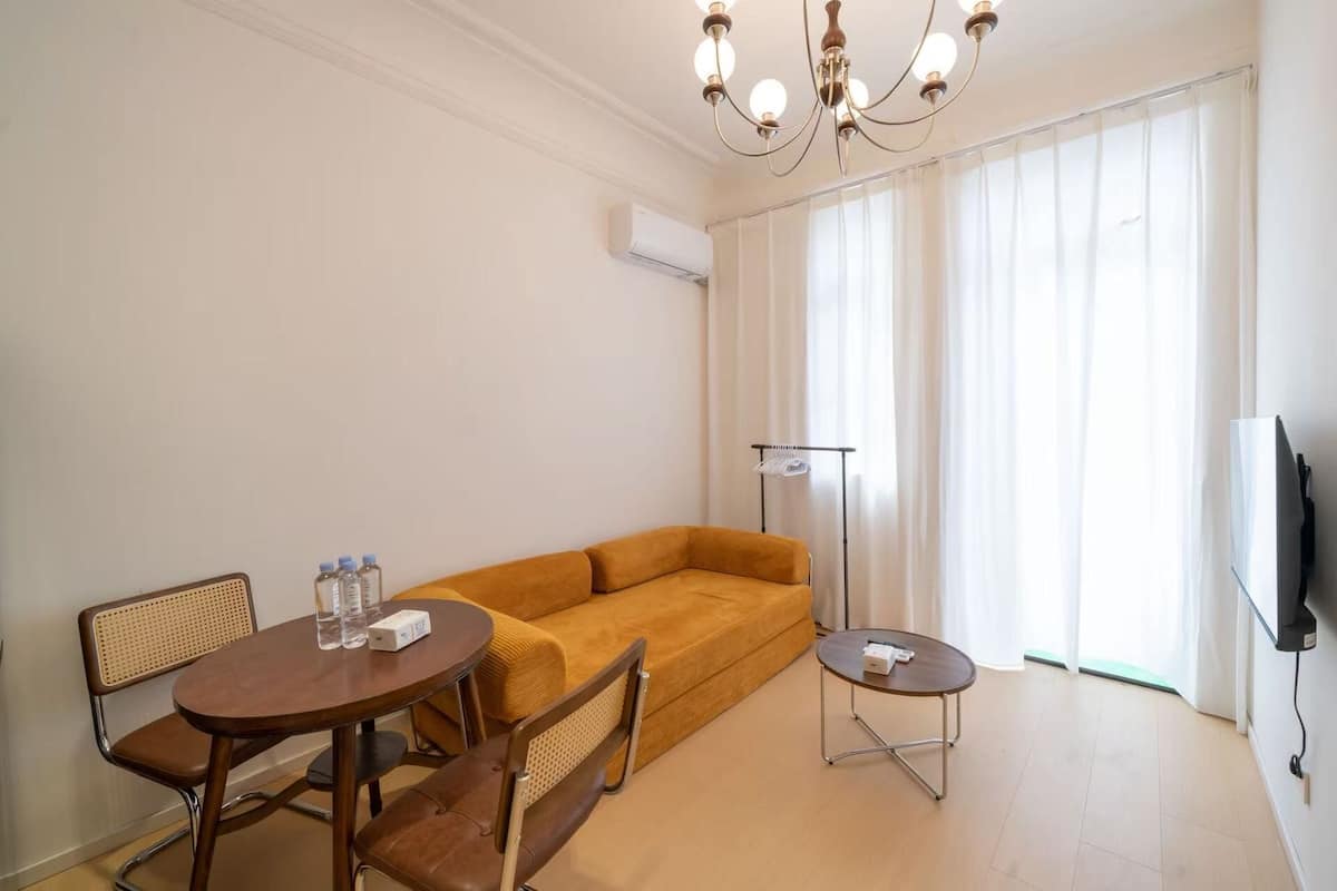 A modern living room with a sofa, a dining table with chairs, a floor lamp, and a TV.