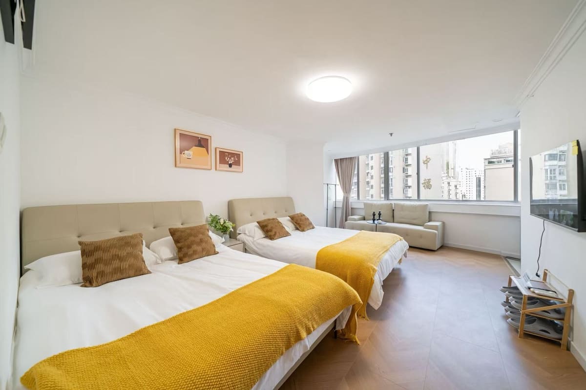 A hotel room with two beds, a sofa, a TV, and a window with a city view.