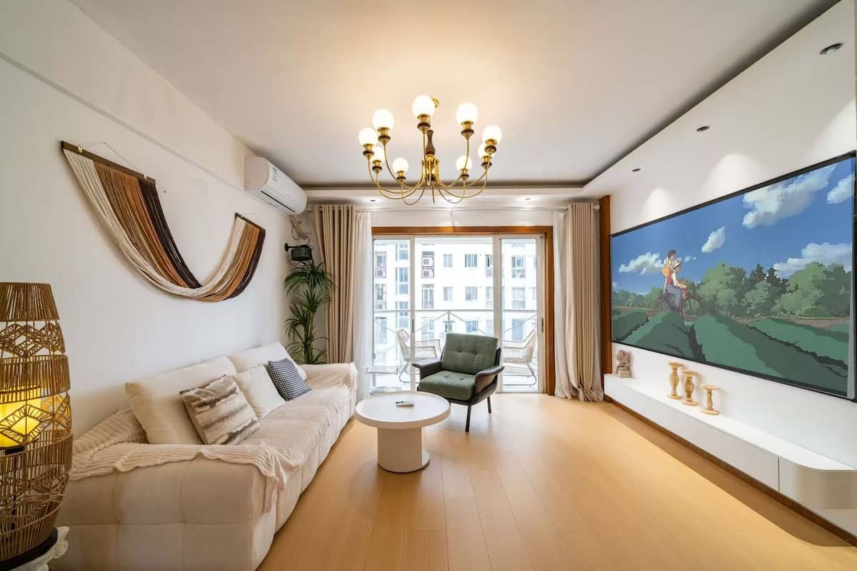 A living room with a sofa, a chair, a coffee table, a chandelier, and a large TV screen.