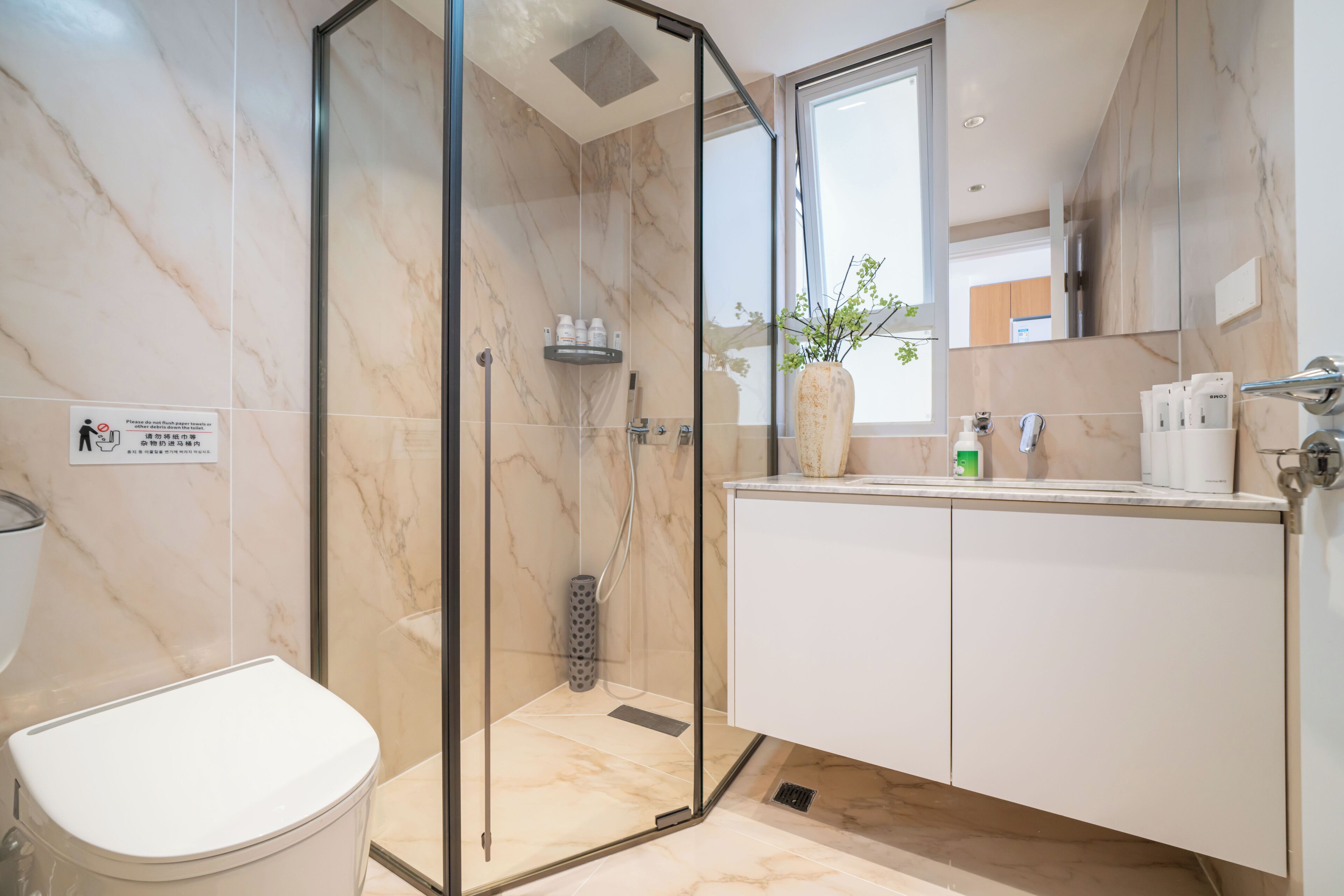 Une salle de bain moderne avec une douche à parois de verre, des toilettes, un lavabo avec un miroir et un vase de fleurs.