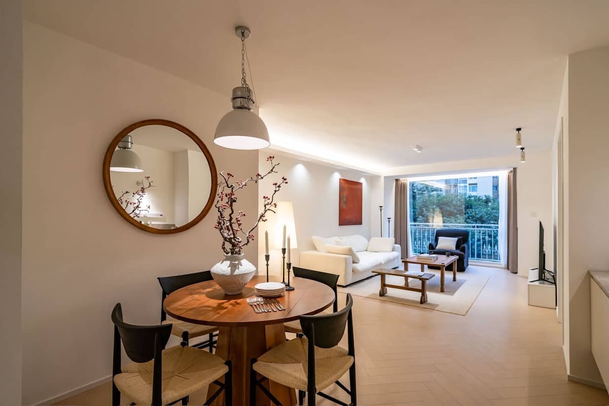 A modern living room with a dining area, a large mirror, and a view of the outdoors.