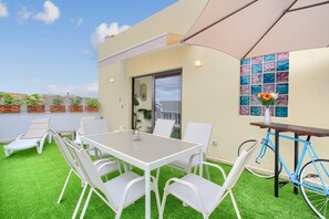 A rooftop terrace with a table and chairs, a bicycle, and potted plants.